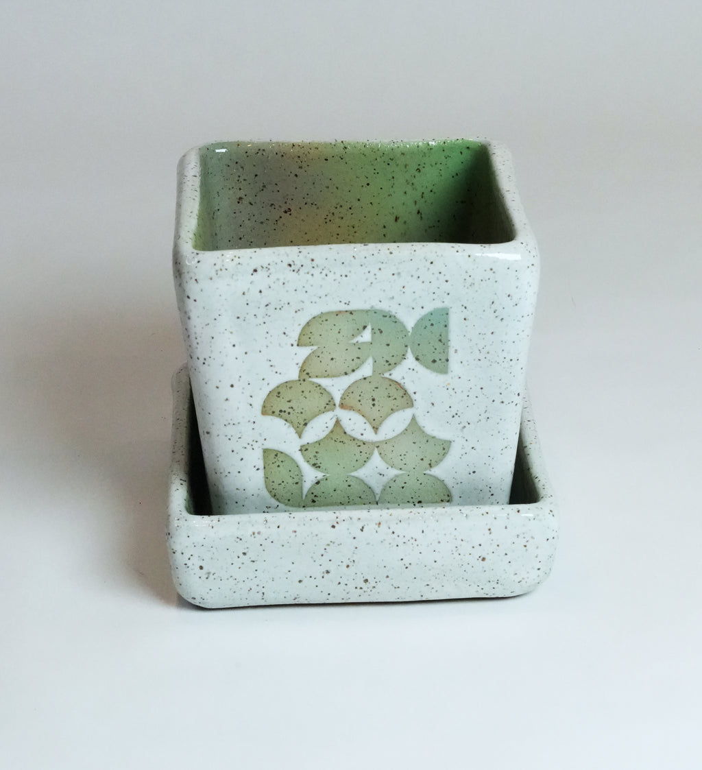 Speckled green ceramic planter with decorative design on a white background